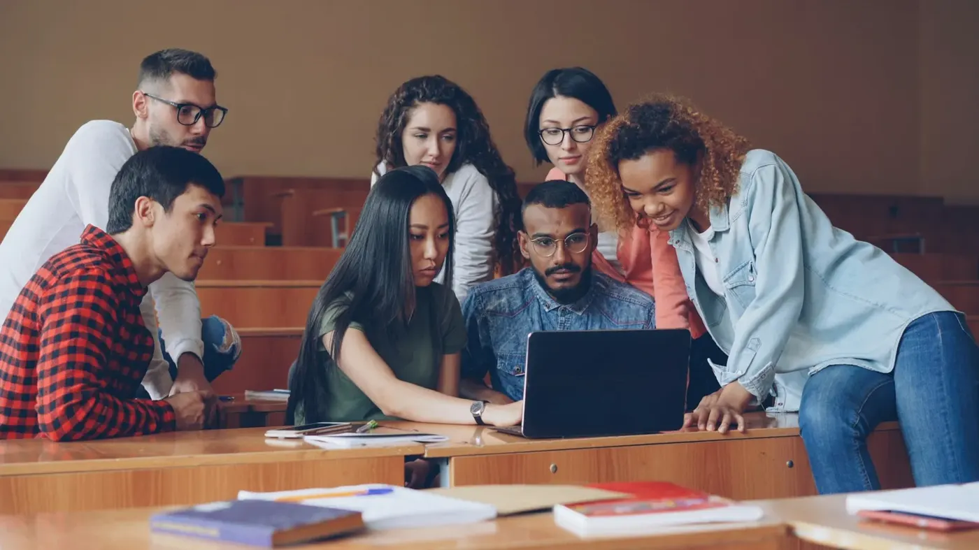 Students working together around a laptop in a lecture hall