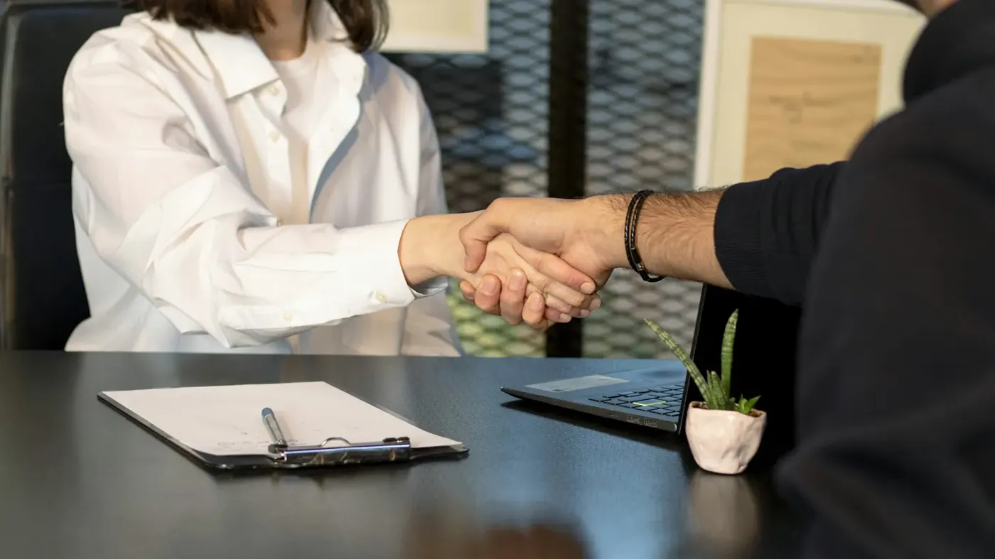 Two people shaking hands across a desk at a job interview