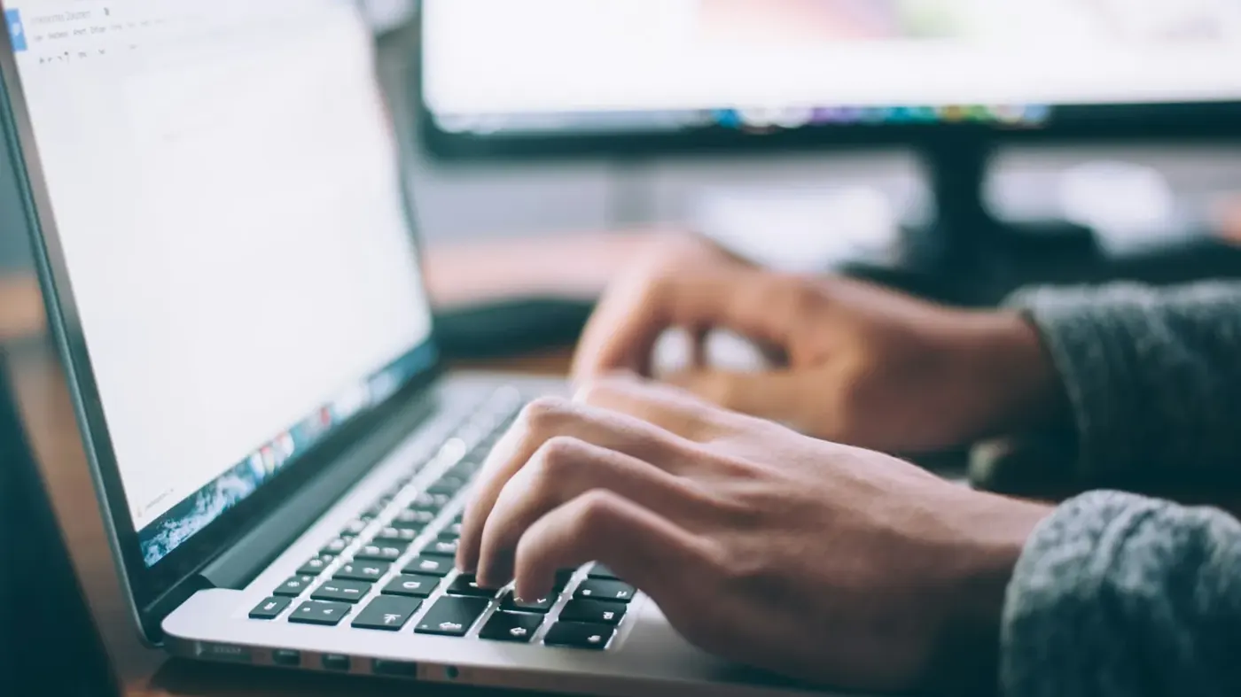 Person writing on a laptop at a desk