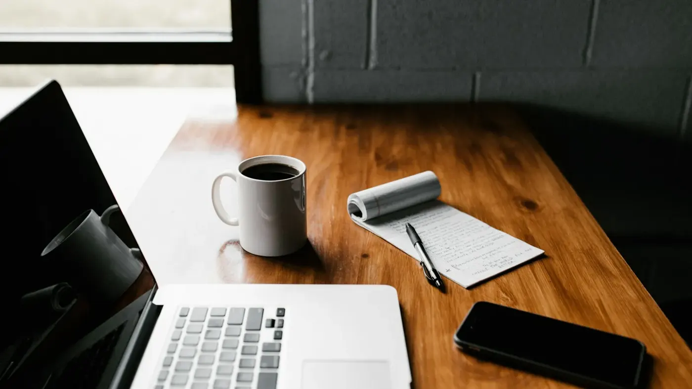 A laptop, phone and coffee mug on a work desk