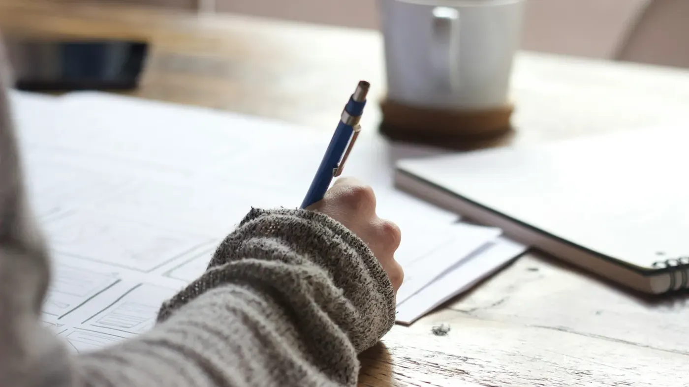 A person writing notes at a wooden desk